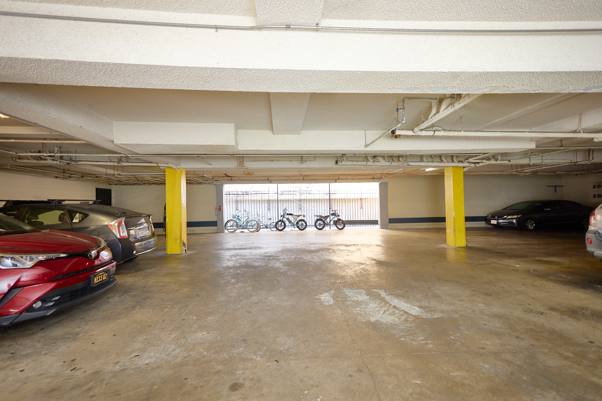 A parking garage with a red car on the left and a black car on the right.
